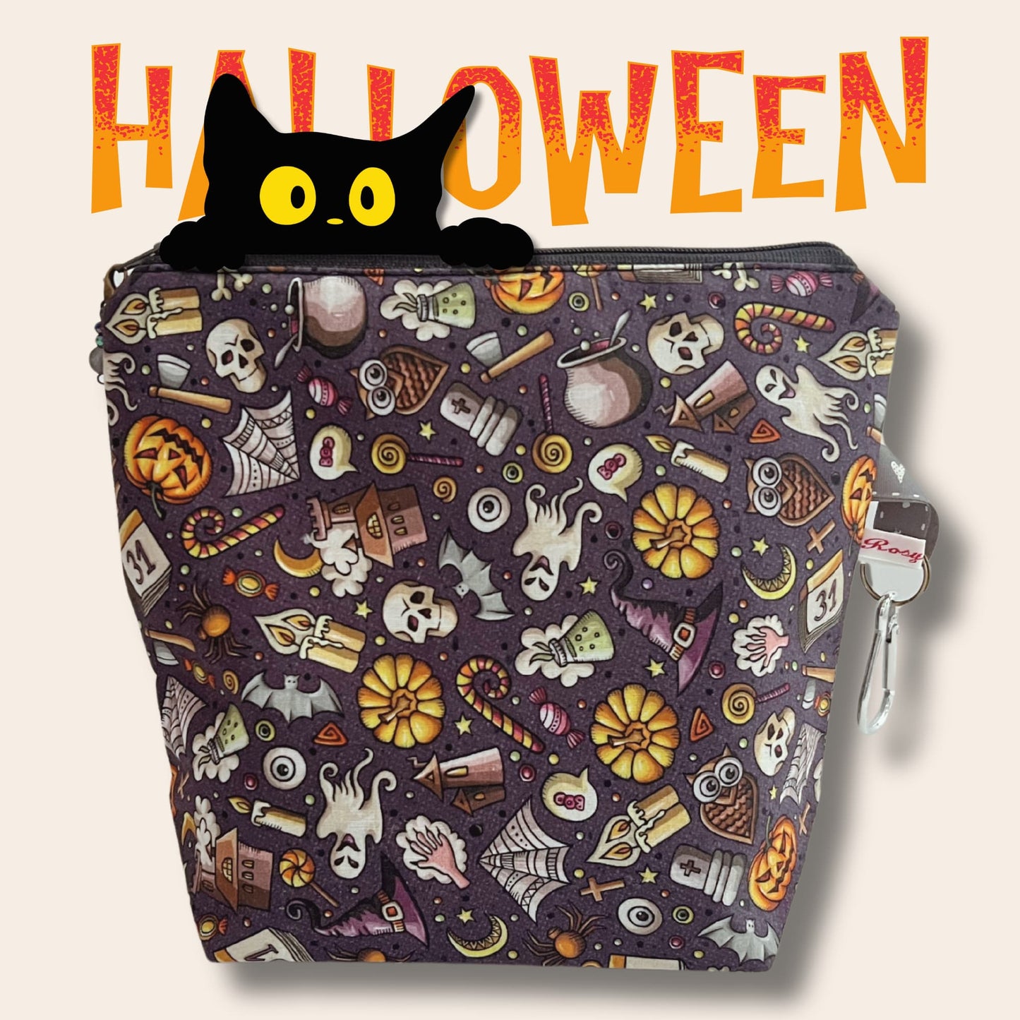 A dark grey bag covered in cartoon Halloween illustrations. A black cat peeks over the top in front of "Halloween".